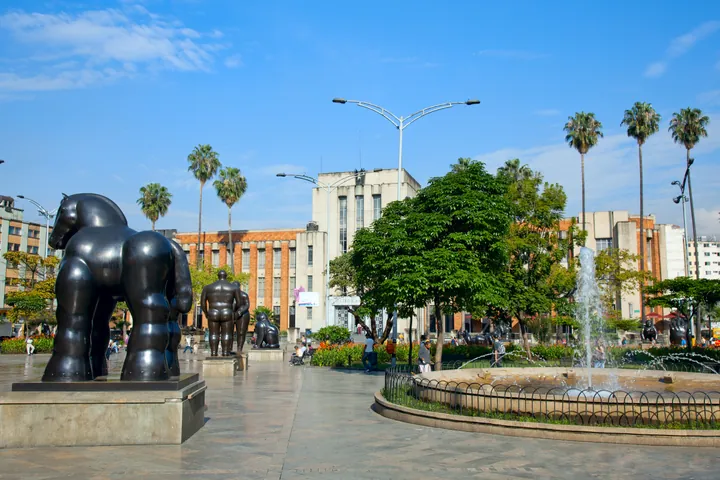 Una escultura de bronce de Fernando Botero en la plaza, entre palmeras y visitantes.