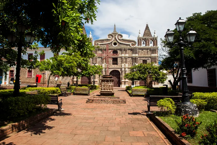 Una iglesia colonial de Santa Fe de Antioquia vista desde el parque, entre árboles y faroles.
